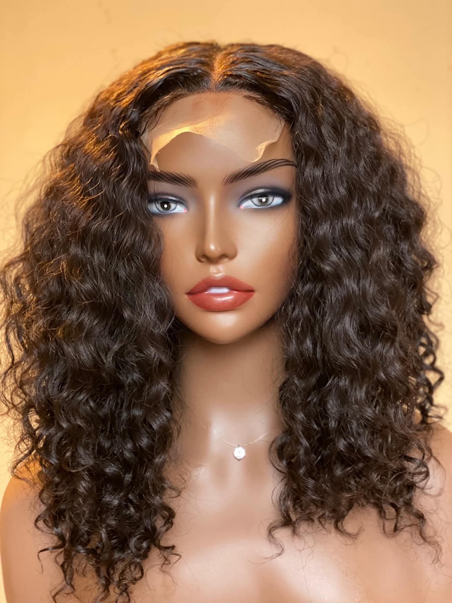 Mannequin head with a curly brown wig on a beige background