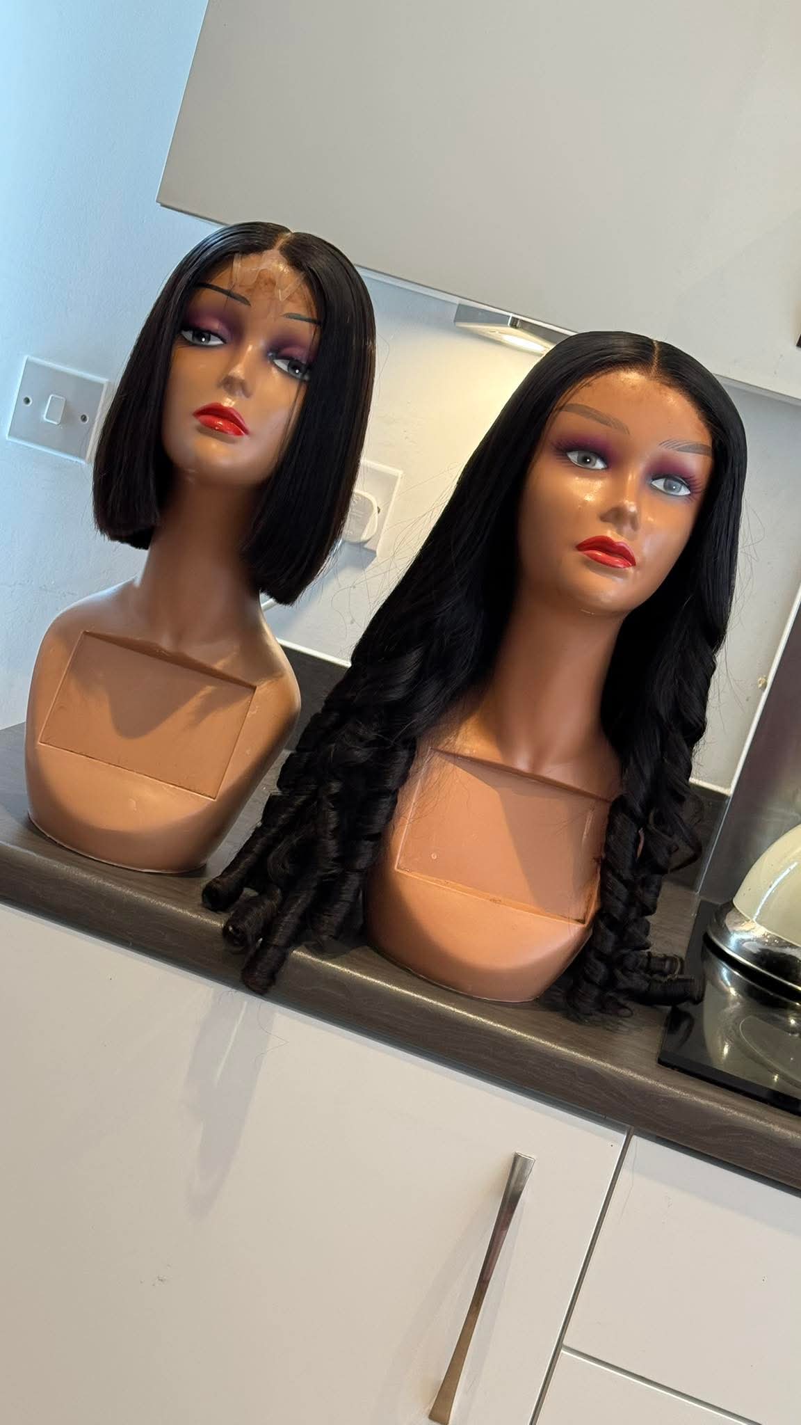 Two mannequin heads with wigs on a kitchen counter.